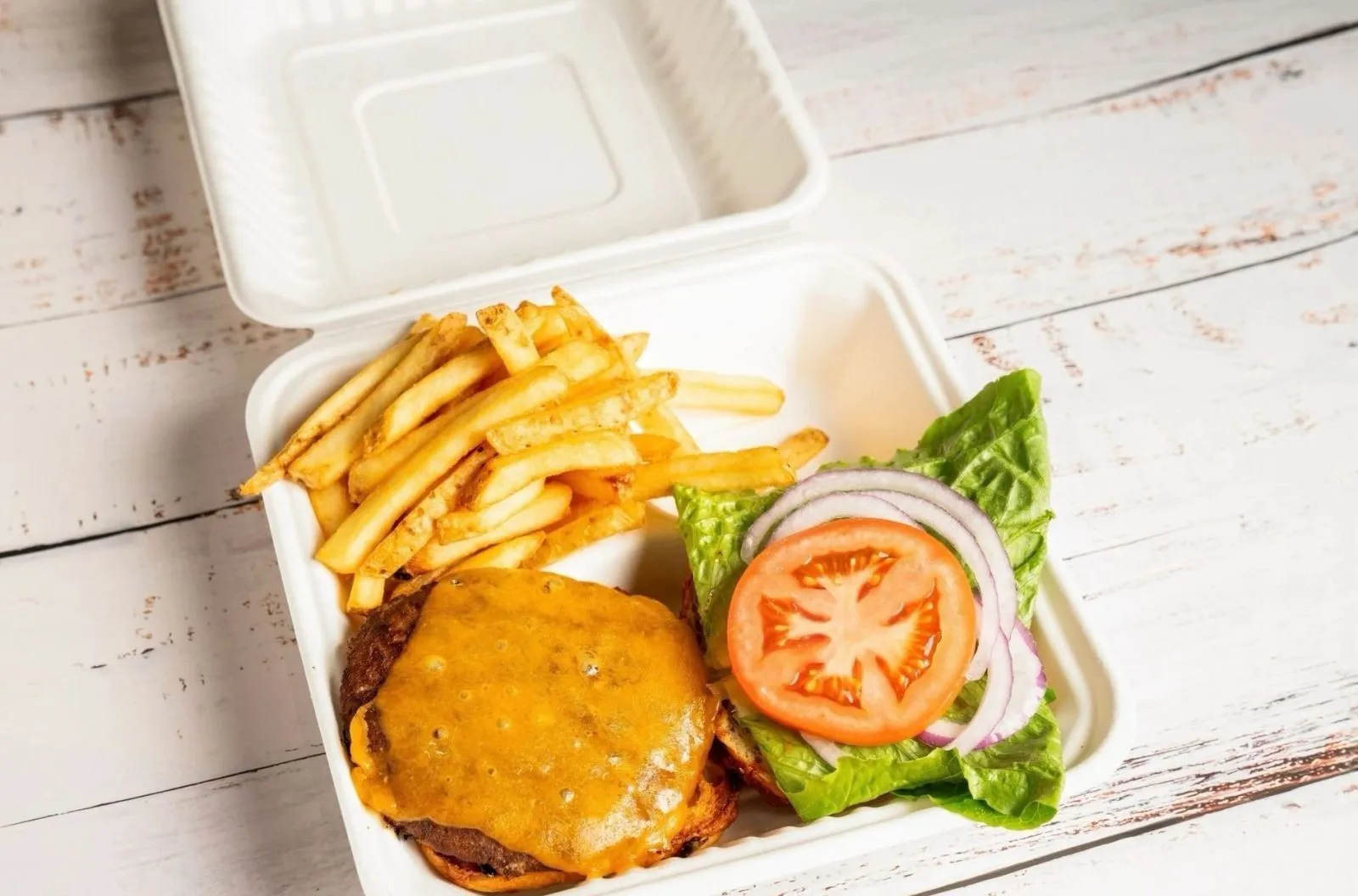 A fresh cheeseburger and fries in a takeout box on a weathered table